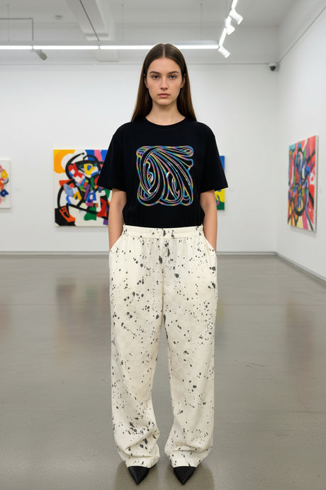 Person wearing a black t-shirt with a colorful design and white pants with black patterns against a plain background