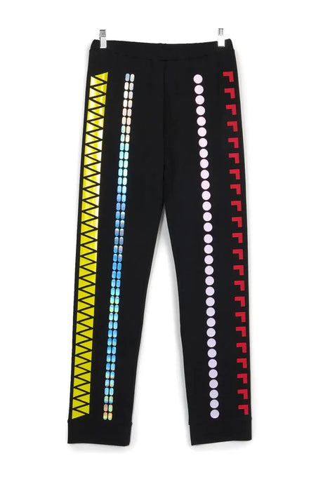 Black pants with colorful geometric prints, including yellow triangles, iridescent ovals, pink circles, and red angles.