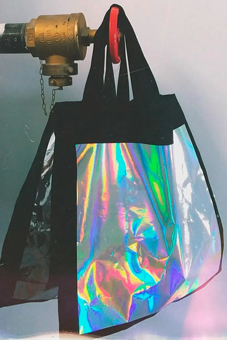 Large black tote bag with shiny holographic front panel hanging on industrial valve