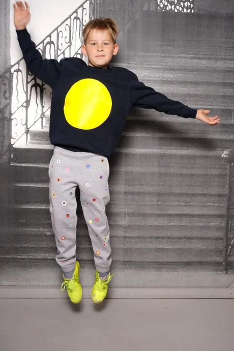 Child jumping in a navy sweater with large yellow circle and grey pants with colorful dots