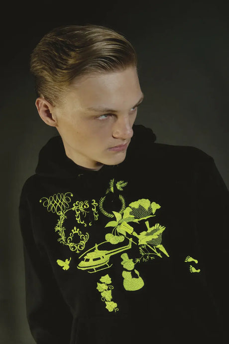 Model wearing black hoodie with neon yellow embroidery, featuring nature and abstract designs