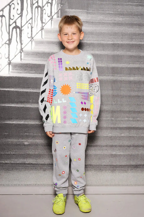 Smiling child wearing a grey sweater and joggers with colorful geometric prints