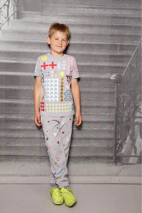 Smiling child wearing a colorful graphic print gray t-shirt and pants set, standing indoors