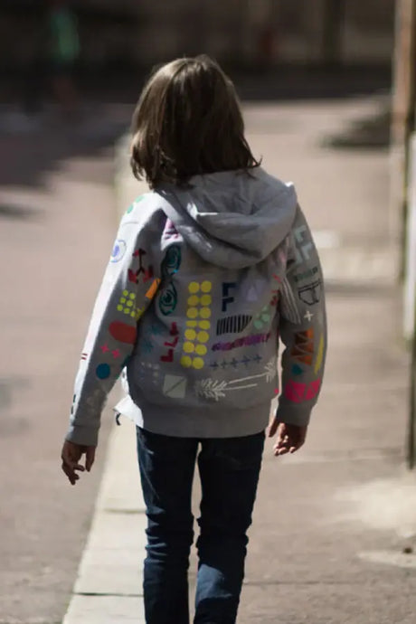 Child wearing grey zip jacket with colorful painted prints, walking outdoors in sunlight
