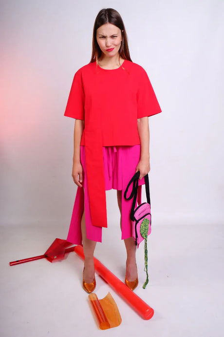 Woman in bright red blouse and pink skirt, holding a playful bag, studio background