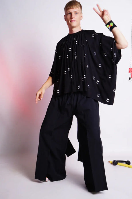Model wearing wide black trousers and black oversized top with white smiley face print