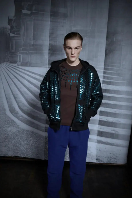Model in shiny sequin zip jacket hoodie with blue pants, urban monochrome background
