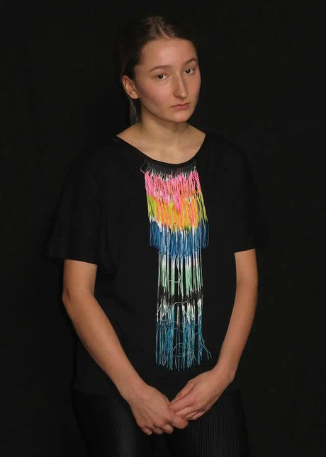 Model wearing black t-shirt with colorful fringe chain accessory on chest, black background