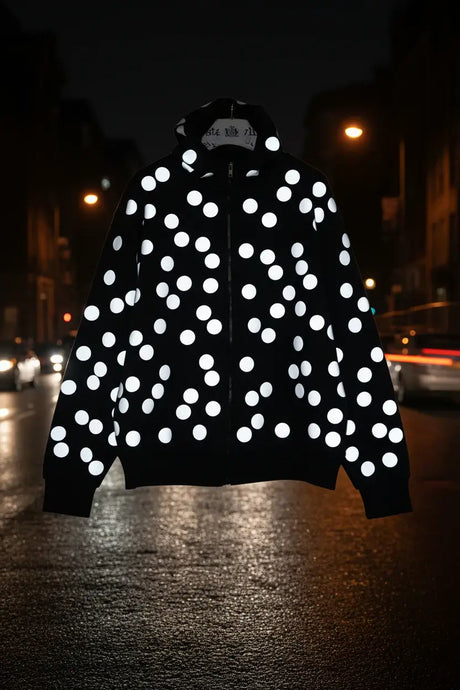 Black zip jacket with large white reflective polka dots, displayed at night on a city street.