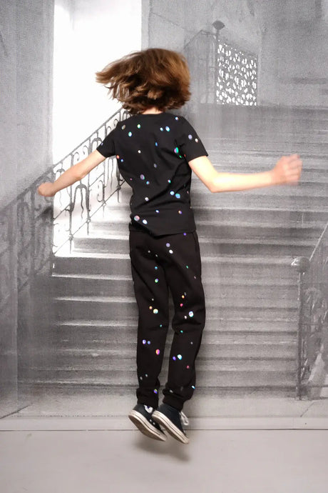 Kid jumping in black joggers and t-shirt with colorful holographic dots