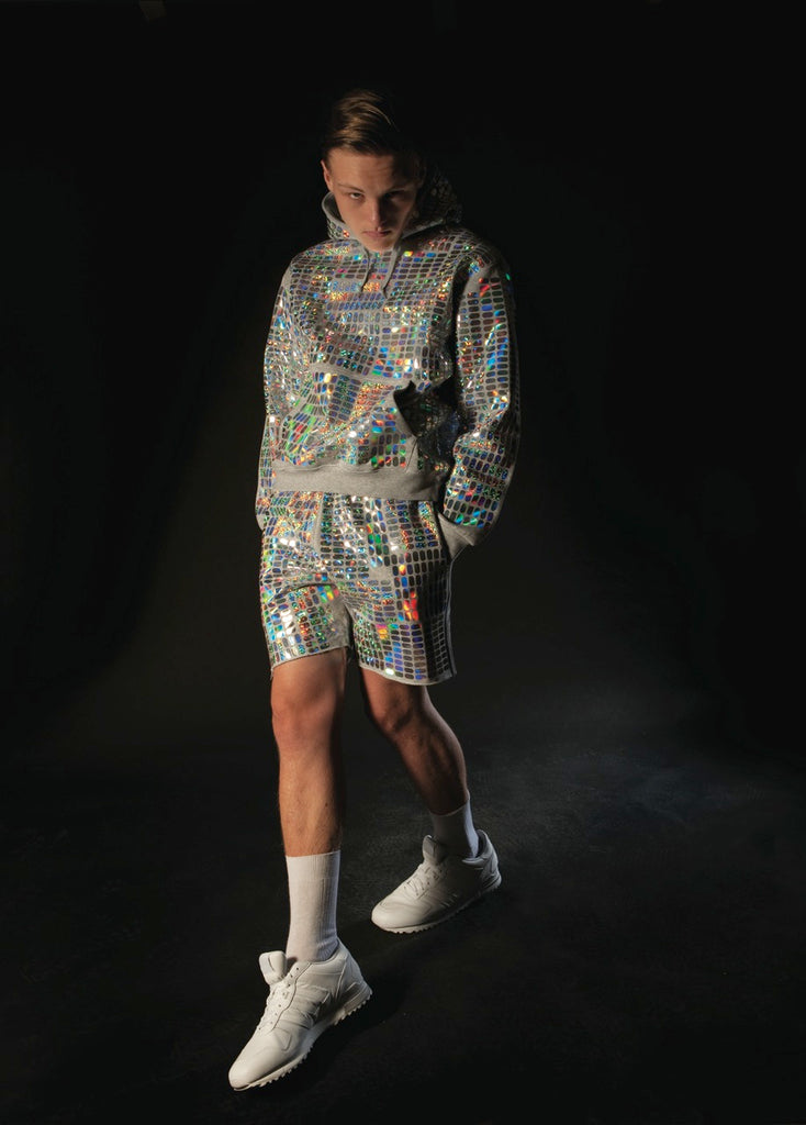 model wearing a grey hoody and shorts with holographic print all over, similar to a disco ball