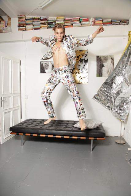 Model jumps on bench wearing colorful graphic print jacket and pants in modern studio room