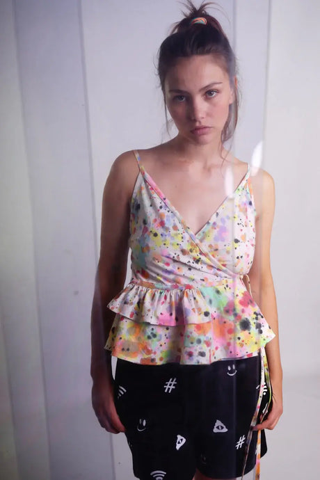 Woman wearing colorful hand-painted peplum top and black shorts with white graphic symbols