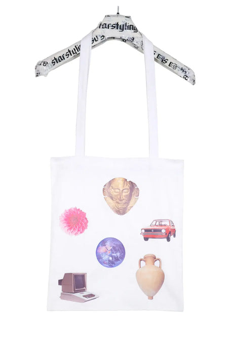 White tote bag with colorful collage prints including a gold mask, red car, globe, pink flower, vintage computer, and ceramic vase, hanging on a branded hanger.