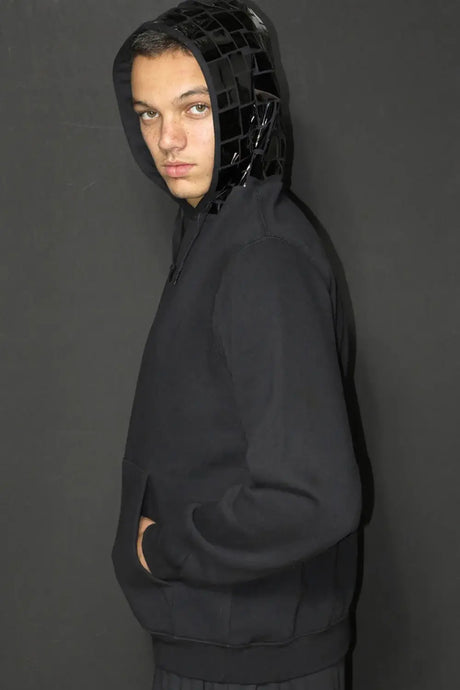Model wearing black hoodie with glossy mosaic tile hood against dark background