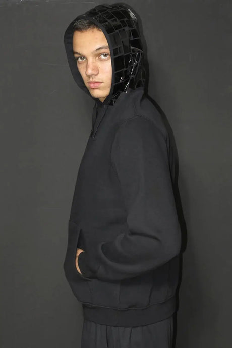 Model wearing black hoodie with glossy mosaic hood, streetwear fashion against dark background