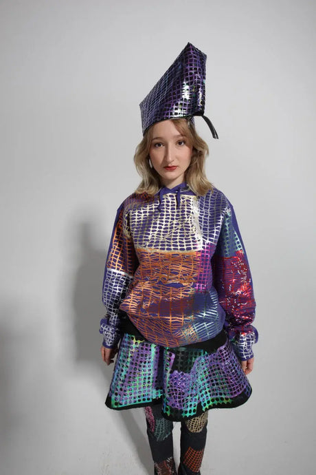 Model wearing colorful foil graphic hoodie, matching skirt, and unique geometric hat