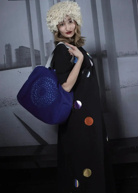 Woman in black floor-length dress with colorful dots, shaggy hat, carrying large blue bag