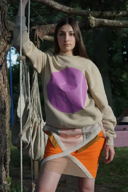 Woman outdoors wearing a beige sweatshirt with purple circle and layered orange skirt