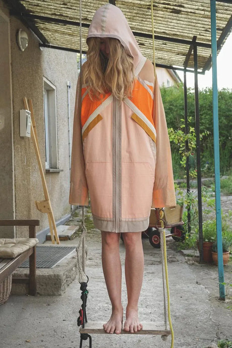 Person wearing hooded pastel and orange sporty coat standing barefoot on a swing outdoors