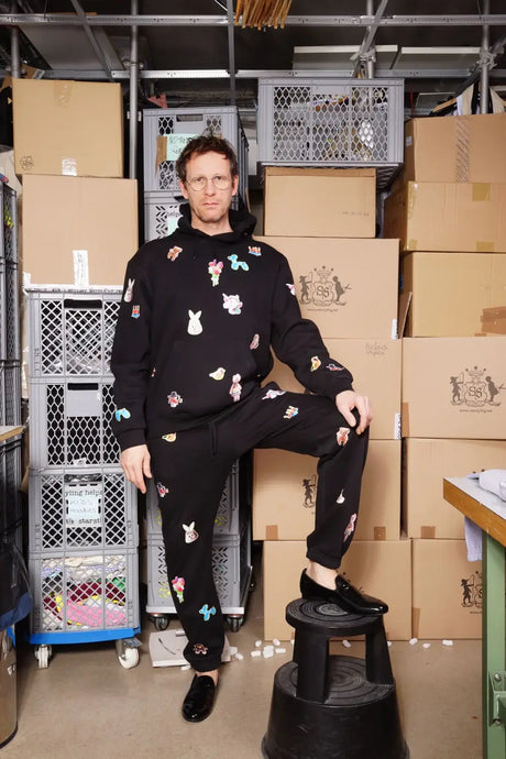 Man wearing black hoodie and sweatpants with colorful animal prints, standing in warehouse