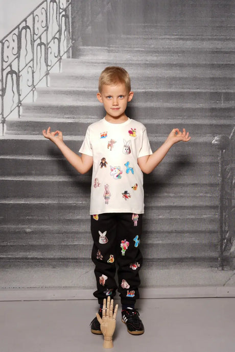 Child wearing white t-shirt and black joggers with colorful cartoon patches, indoor setting