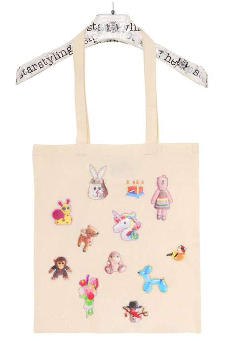 Beige tote bag with colorful animal, toy, and flower sticker prints, hanging on a hanger.