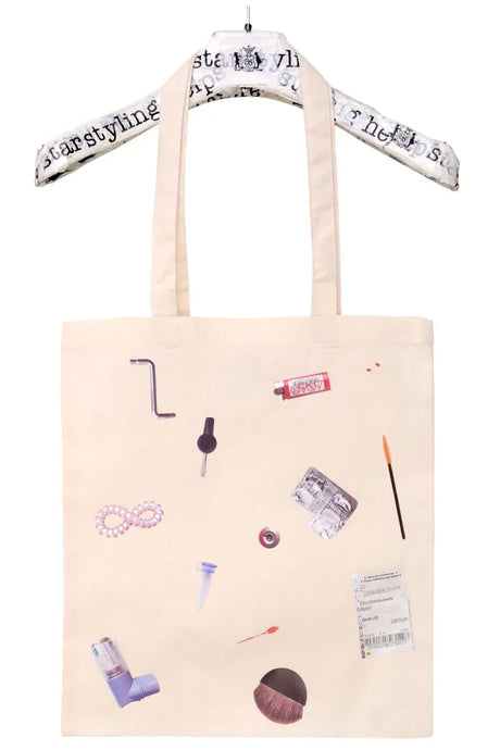Beige tote bag with assorted everyday object prints, hanging on a padded hanger.