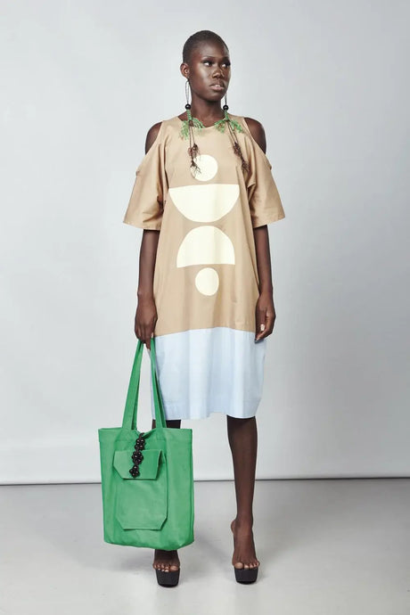 Woman in two-tone midi kaftan dress with abstract print, holding a green tote bag